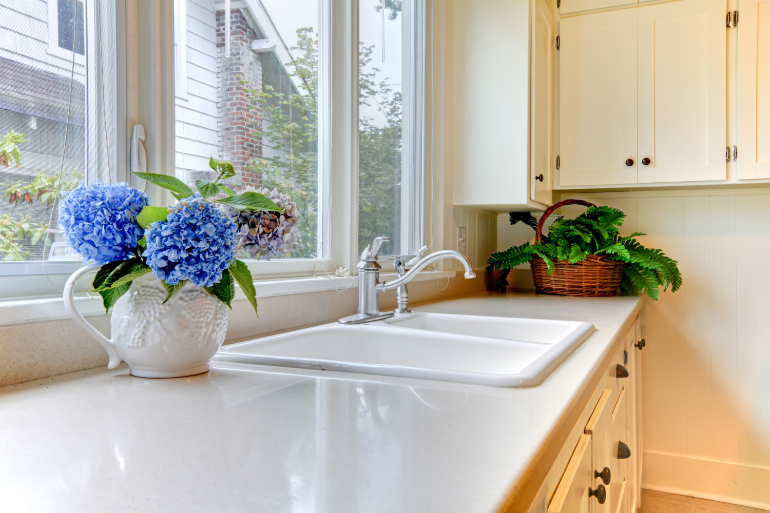 Vase with blue flowers on a white kitchen counter top in front of a window