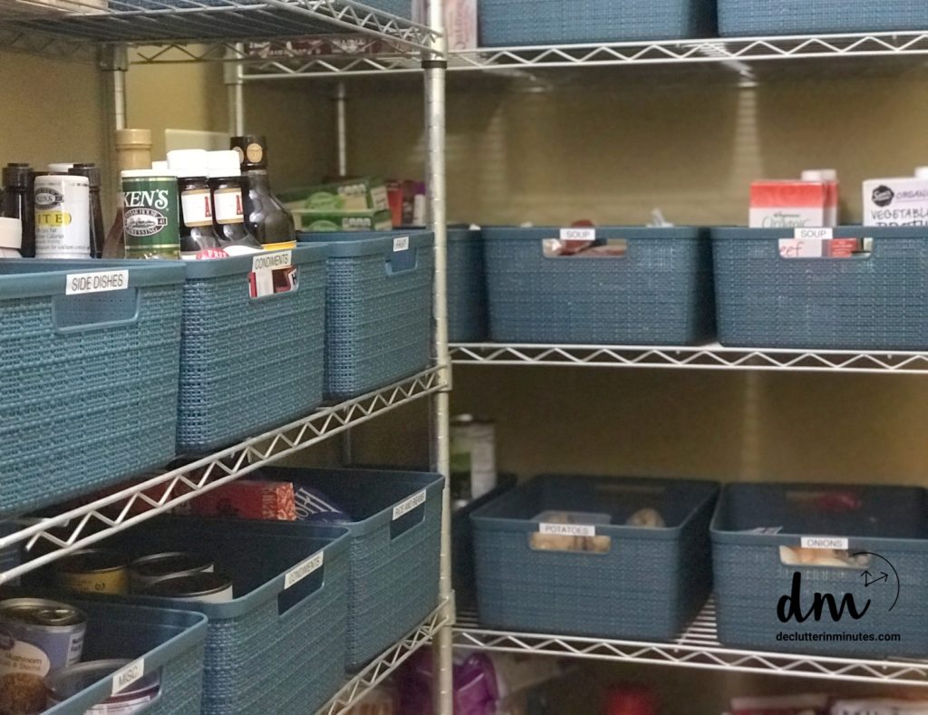 A pantry with labeled blue storage bins on metal shelves, neatly holding condiments, side dishes, soups, and other kitchen essentials