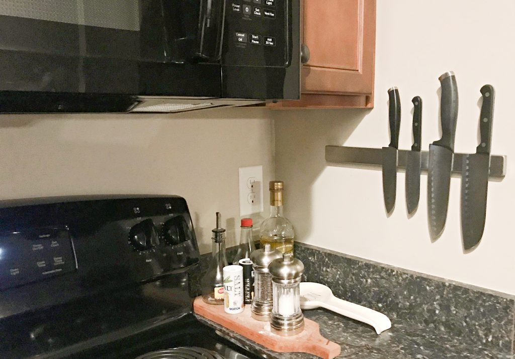A kitchen counter with a magnetic knife strip holding four knives, a stovetop, and a small tray with salt, pepper, and oil bottles