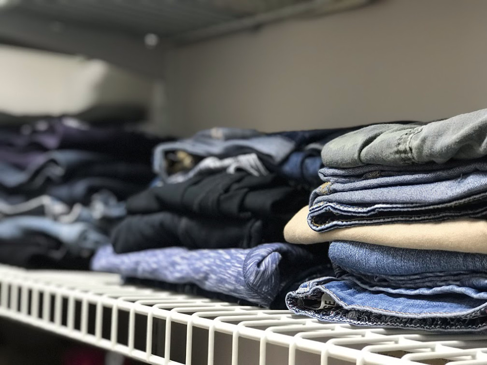 Closet with white organizer rack. Folded pants and jeans stacked ontop of the rack.