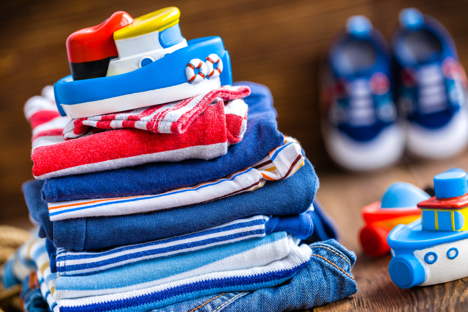 A neatly stacked pile of children's clothes with a toy boat on top, surrounded by nautical-themed items