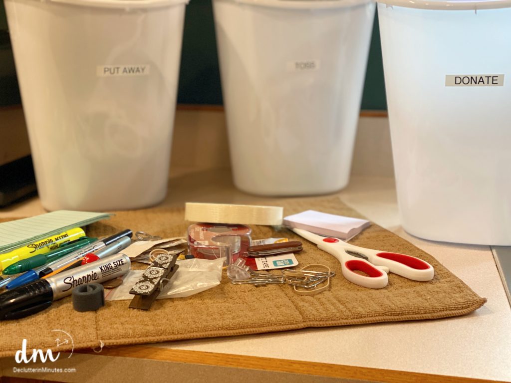 a towel with random items on it with buckets with sorting labels in the background