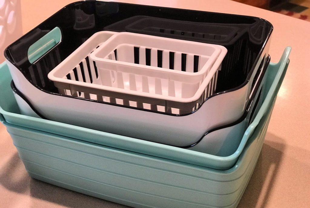 A stack of white, black, and teal basket organizers sitting on a tan kitchen counter.