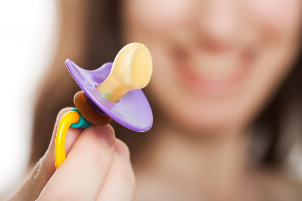 Mother hand holding plastic baby soother pacifier