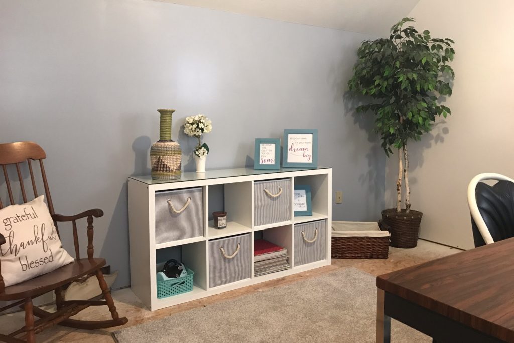 A tidy and organized room featuring a white cubby shelf with storage bins, decorative accents, and a rocking chair with a cozy pillow
