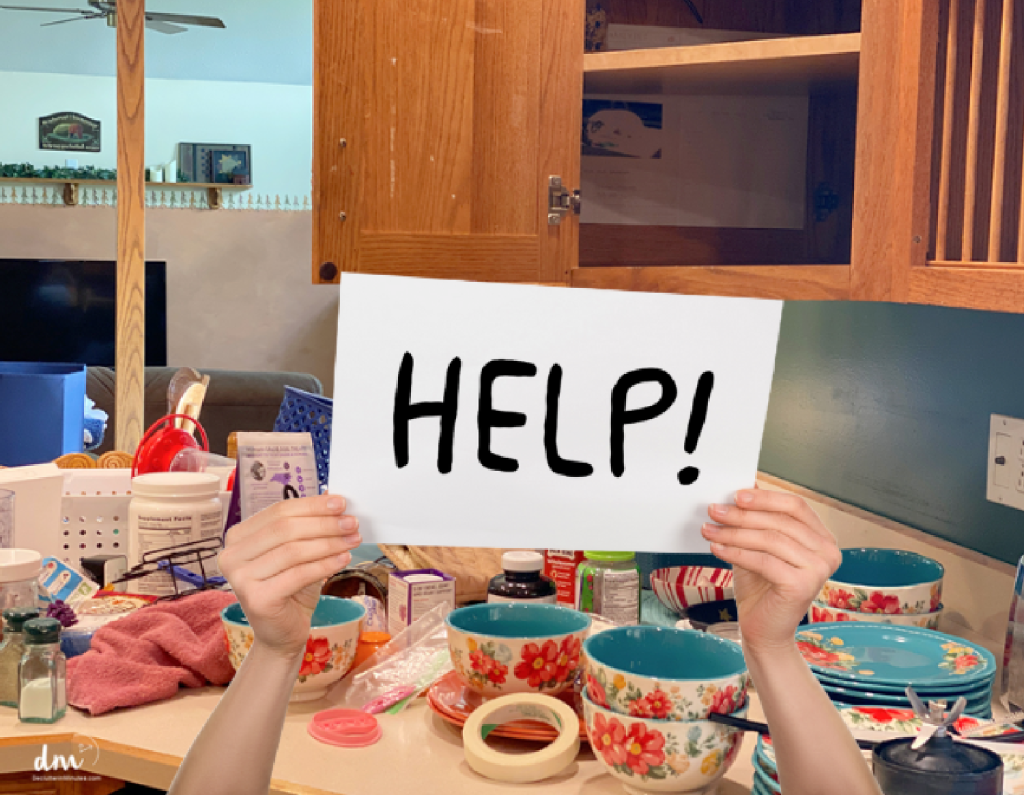 hands holding a HELP sign in front of a messy counter