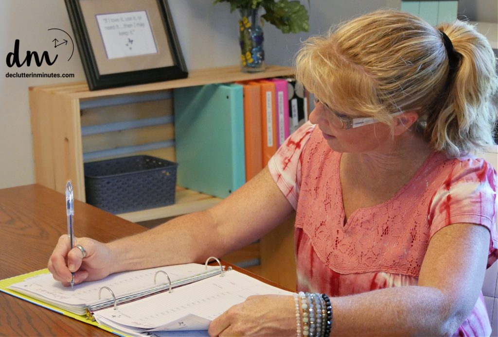 a girl in a pink top writing in a calendar on a desk