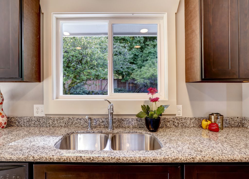 An empty kitchen sink with a pink flower sitting nearby