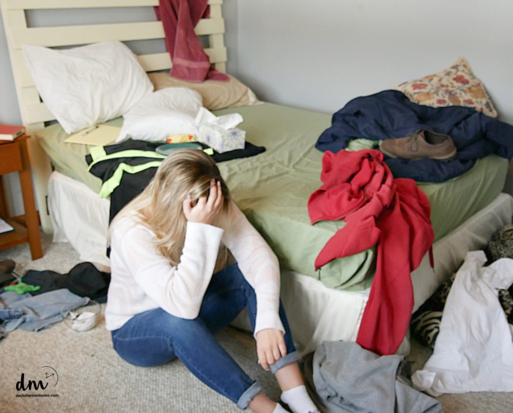 a girl sitting in a messy bedroom head in her hands 