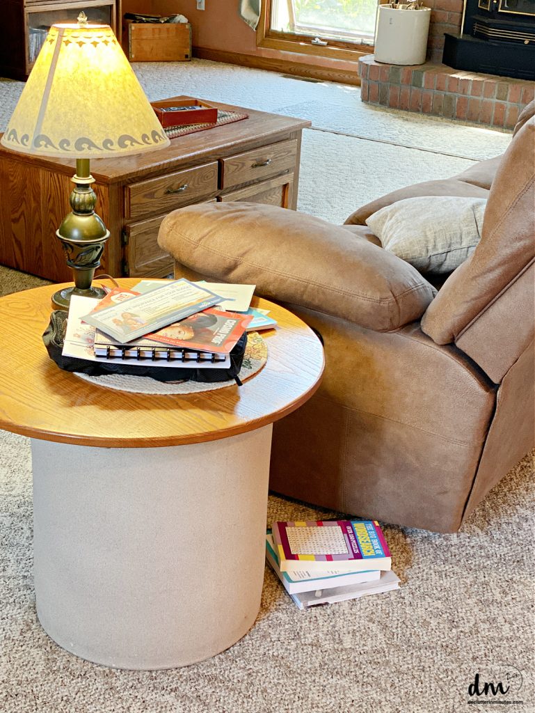 books stacked on the floor near to a chair and end table
