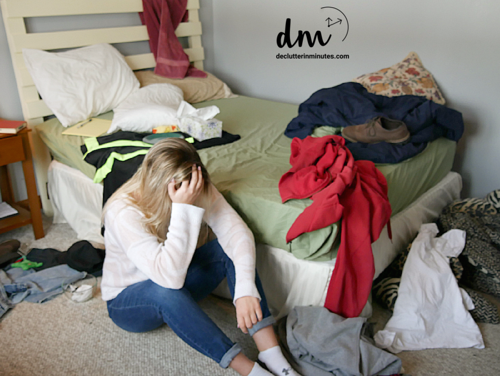 a girl sitting on the floor of a messy bedroom with her head in her hand