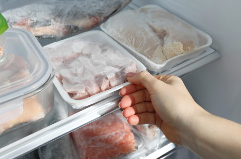 a hand grabbing a container of freezer burned food from a fridge