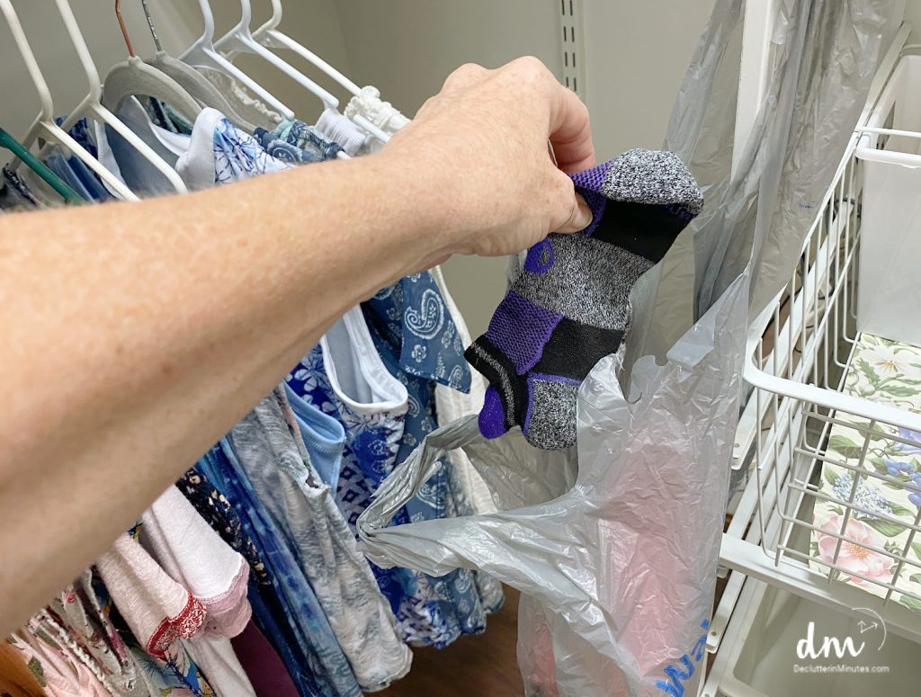 a hand putting socks into a plastic shopping bag in a closet