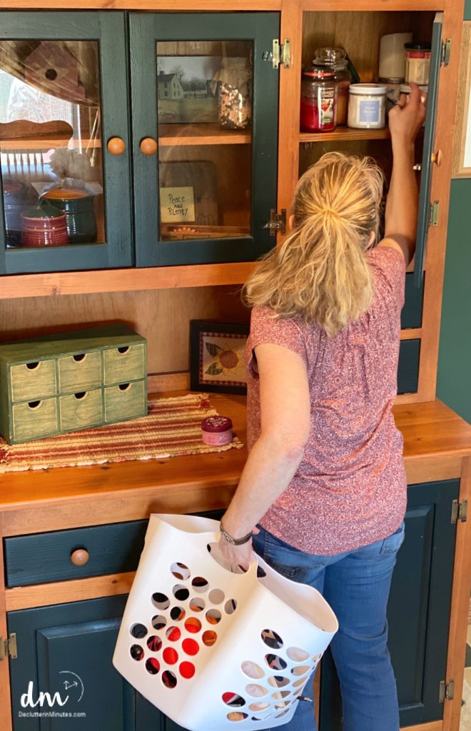 a woman putting things away into a cabinet from a white basket