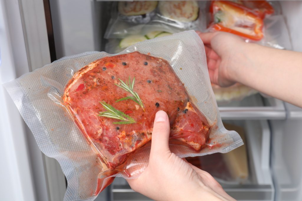 a hand grabbing a container of freezer burned food from a fridge