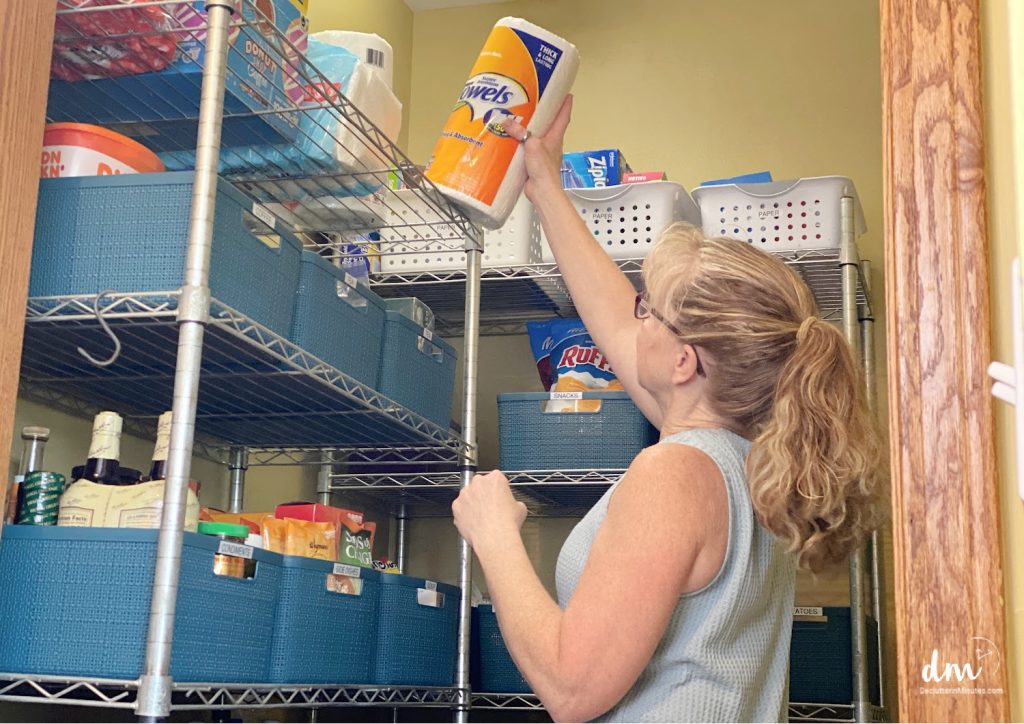a woman putting away a roll of paper towels in a kitchen pantry