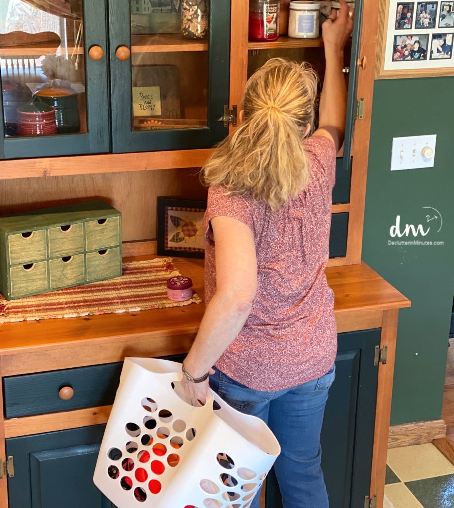 A woman organizing a wooden cabinet while holding a laundry basket