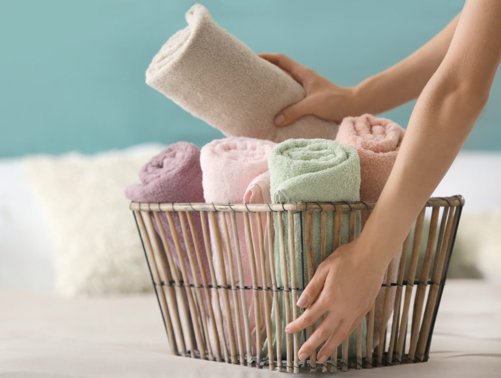 Woman putting clean rolled towels into basket on bed