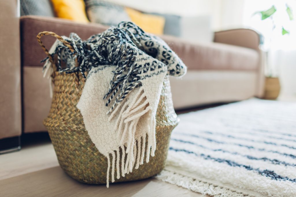 Blanket put in a straw basket by the couch. The interior decor of living room.. 
