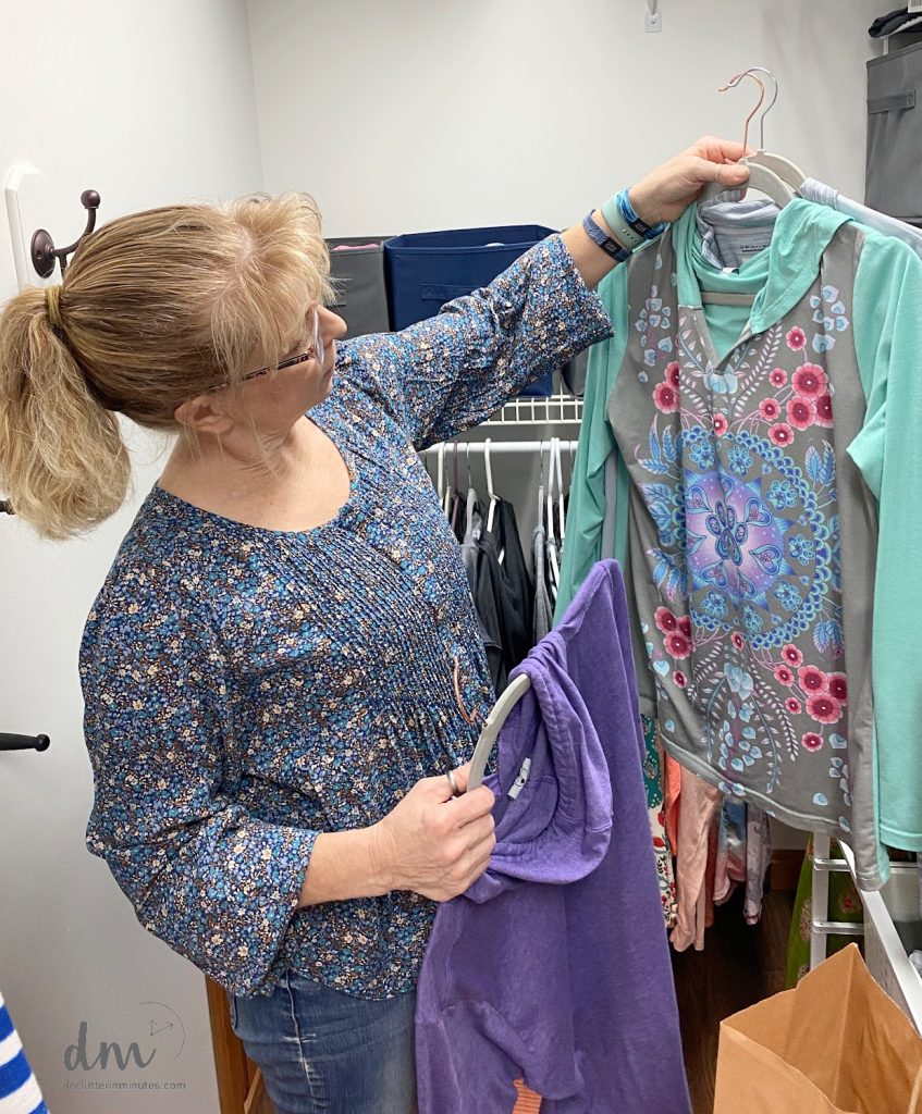 A woman holding up winter shirts to declutter