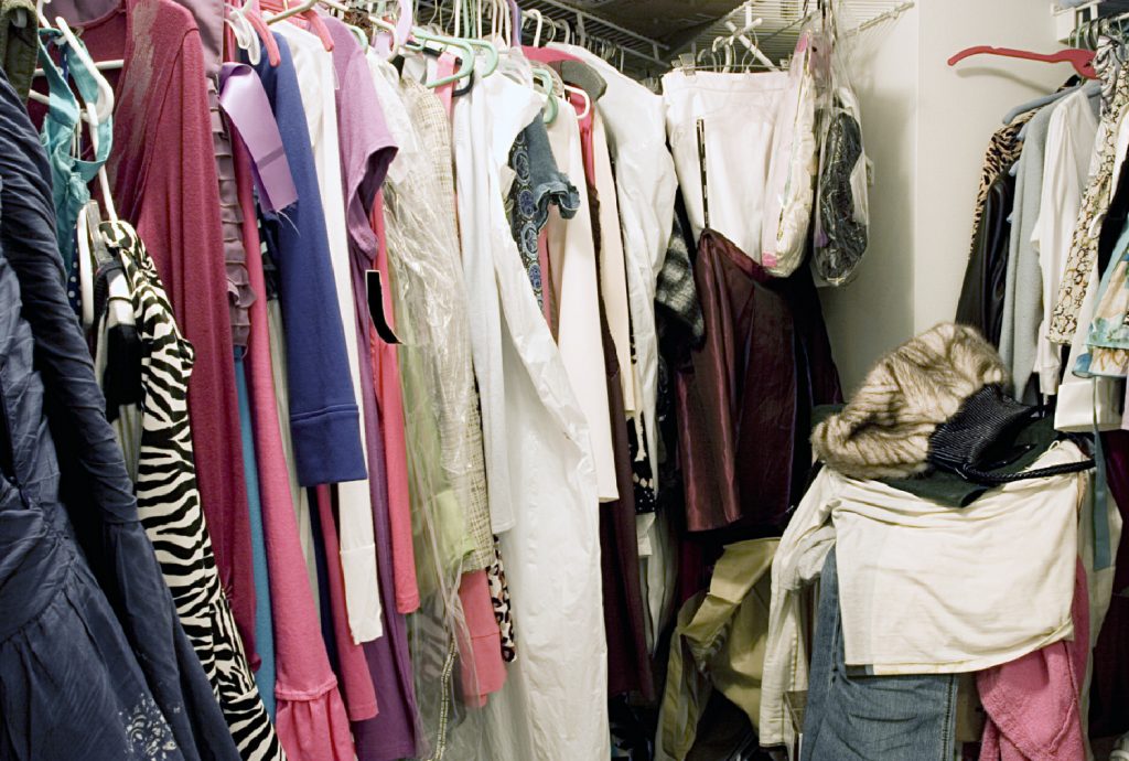 Messy unorganized closet full of hanging clothes