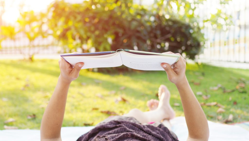 a woman lying on her back in the summer sun reading a book