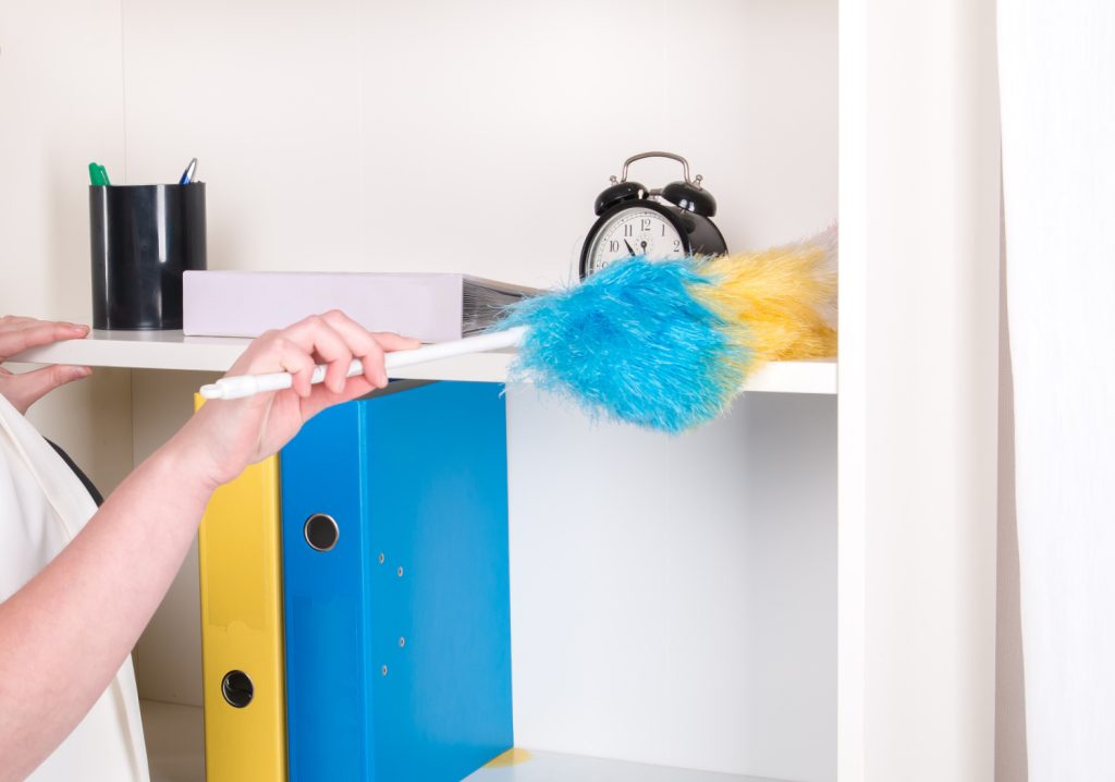hands dusting a shelf with a feather duster