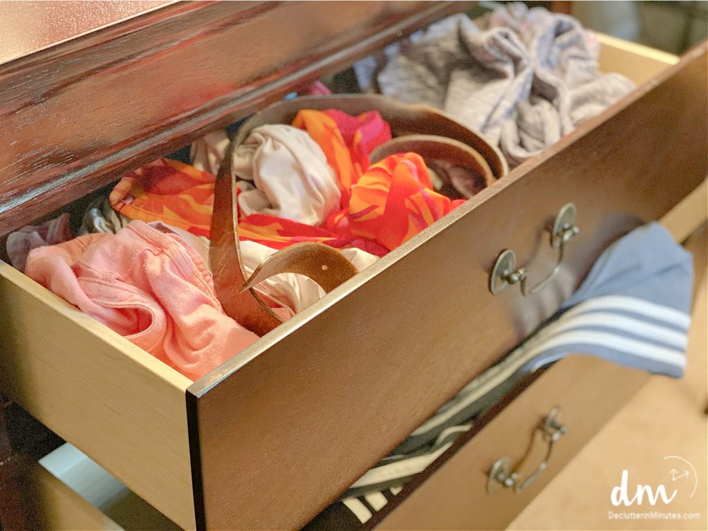 a dresser with opened drawers and messy clothes hanging out