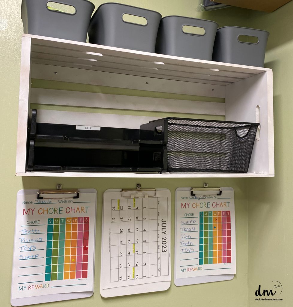 a white shelf on a wall with baskets for papers and 3 clipboards with chore charts