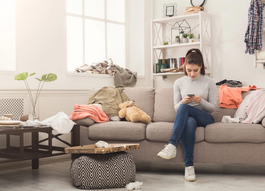 a woman on her phone sitting in a messy and cluttered room 