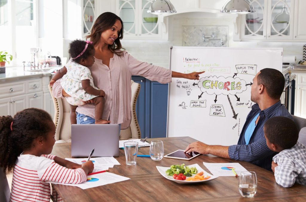 a mom holding a baby talking to her family about chores in the kitchen