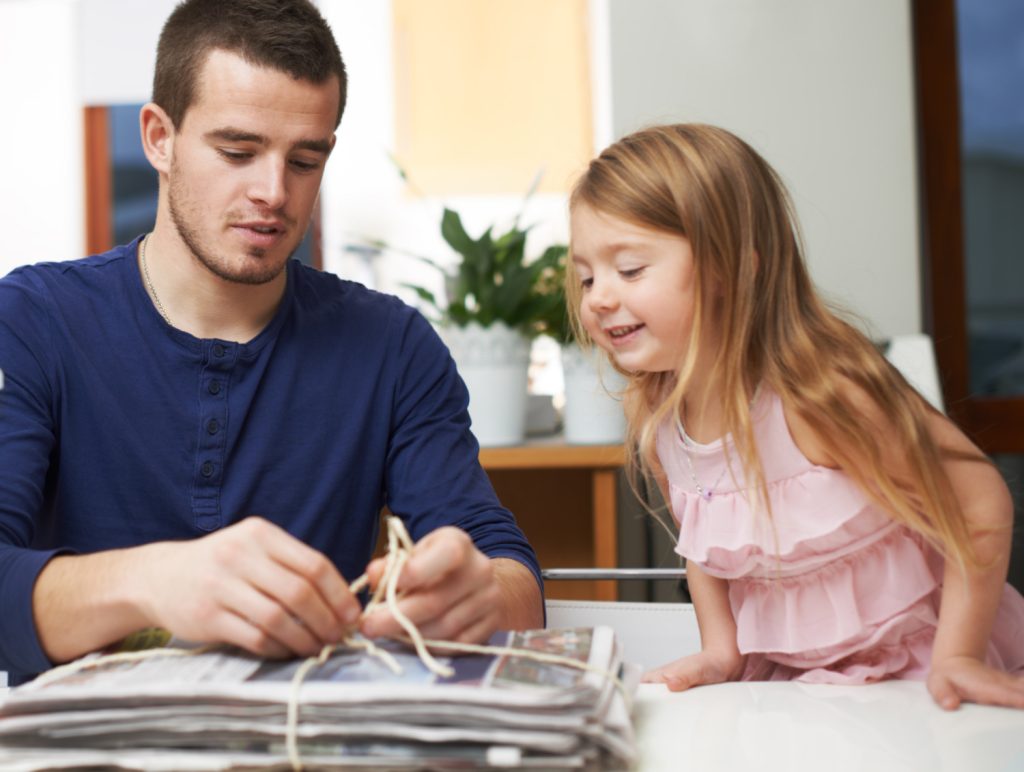 Man tying up newspapers with a young girl watching