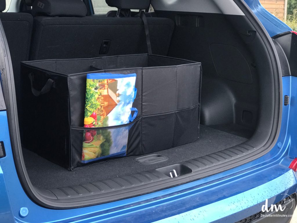 A neatly organized car trunk with a black storage organizer holding reusable grocery bags