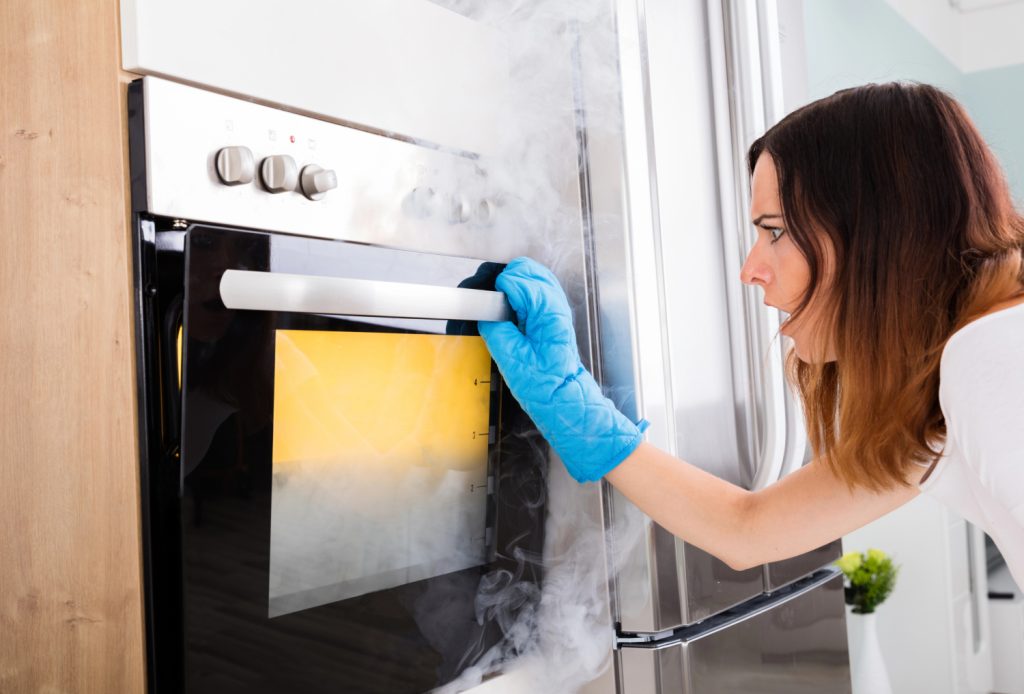 woman looking into an oven with smoke pouring out