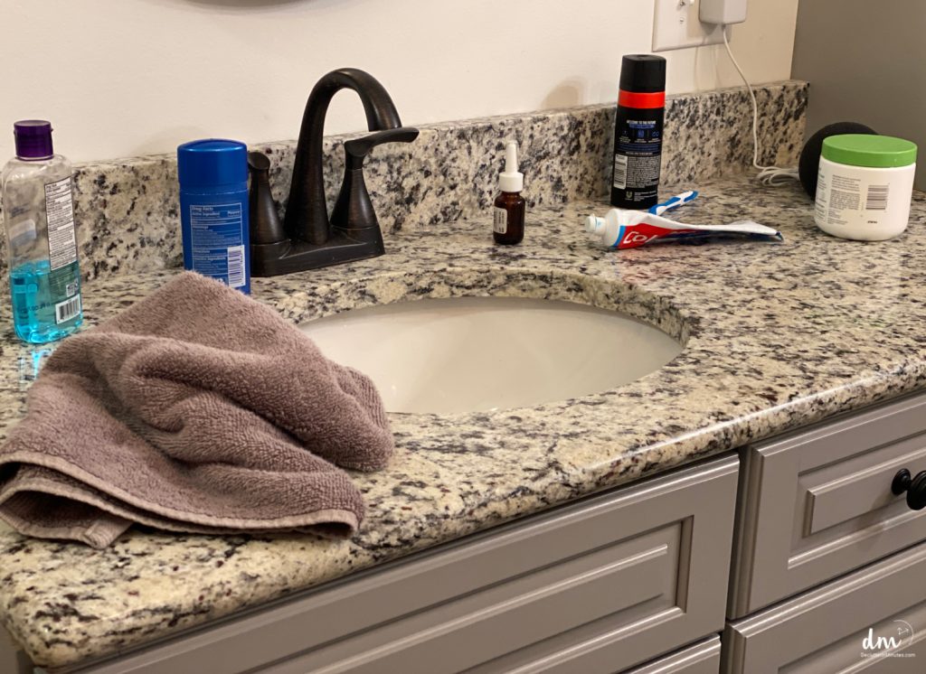 A bathroom sink with a granite countertop, scattered toiletries, and a towel