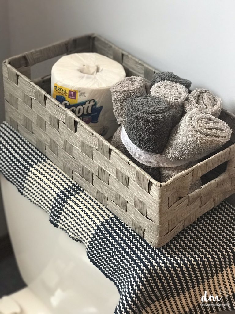 a basket on the back of a toilet with toilet paper and towels