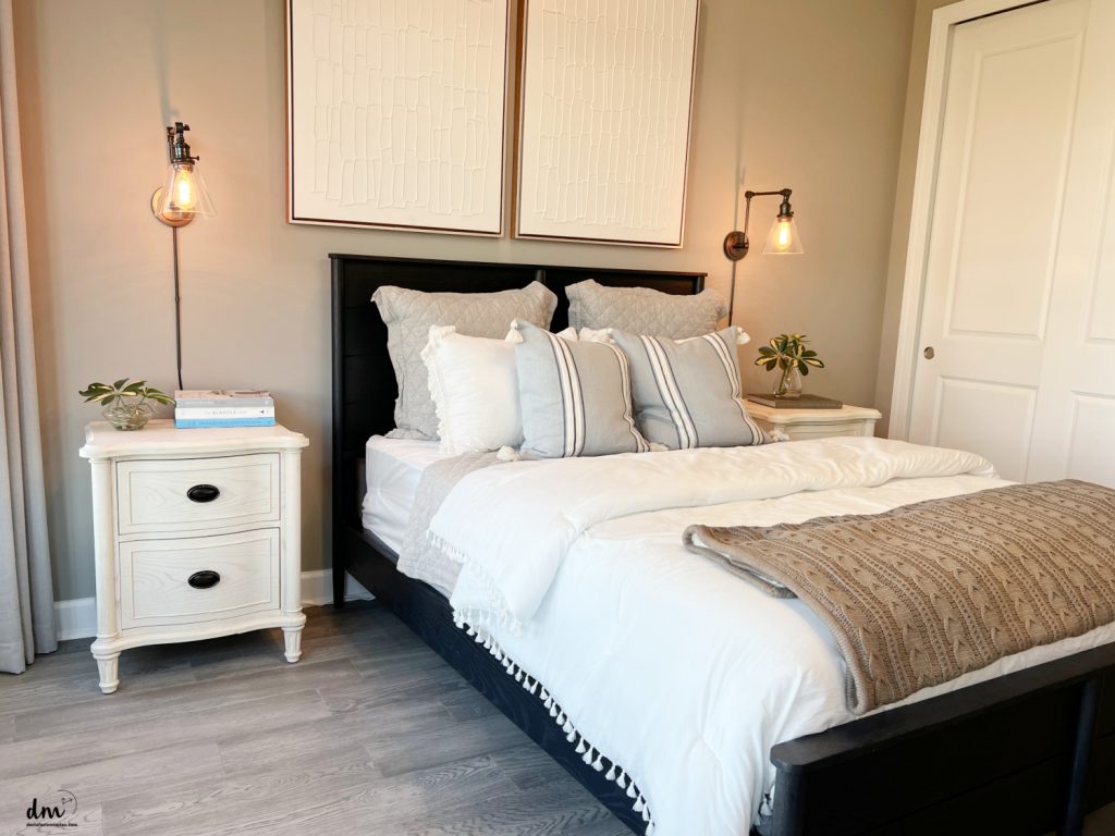 a bed with pillows next to a nightstand with books and a lamp