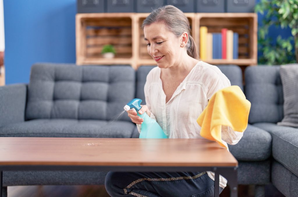 Middle age woman smiling cleaning a coffee table at home