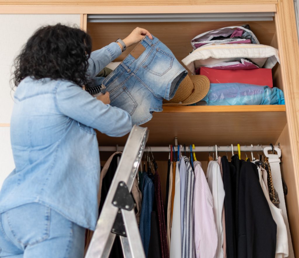 a woman holding shorts standing on a ladder in her closet