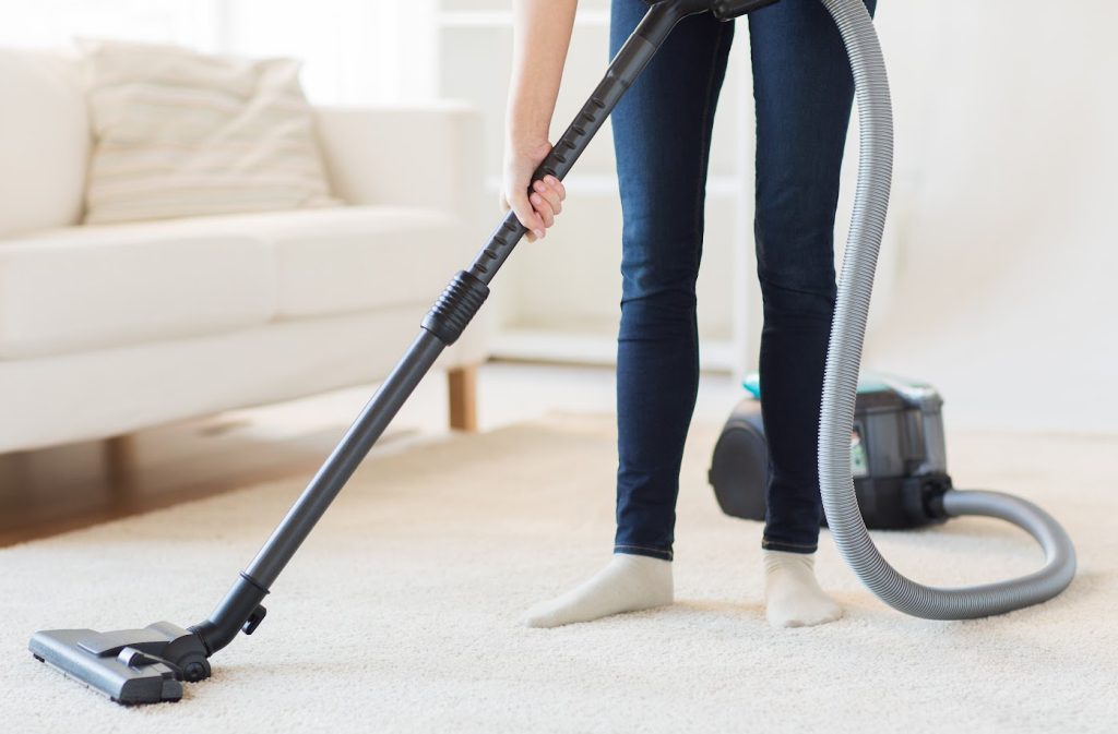 woman vacuuming a carpet in a family room in her socks