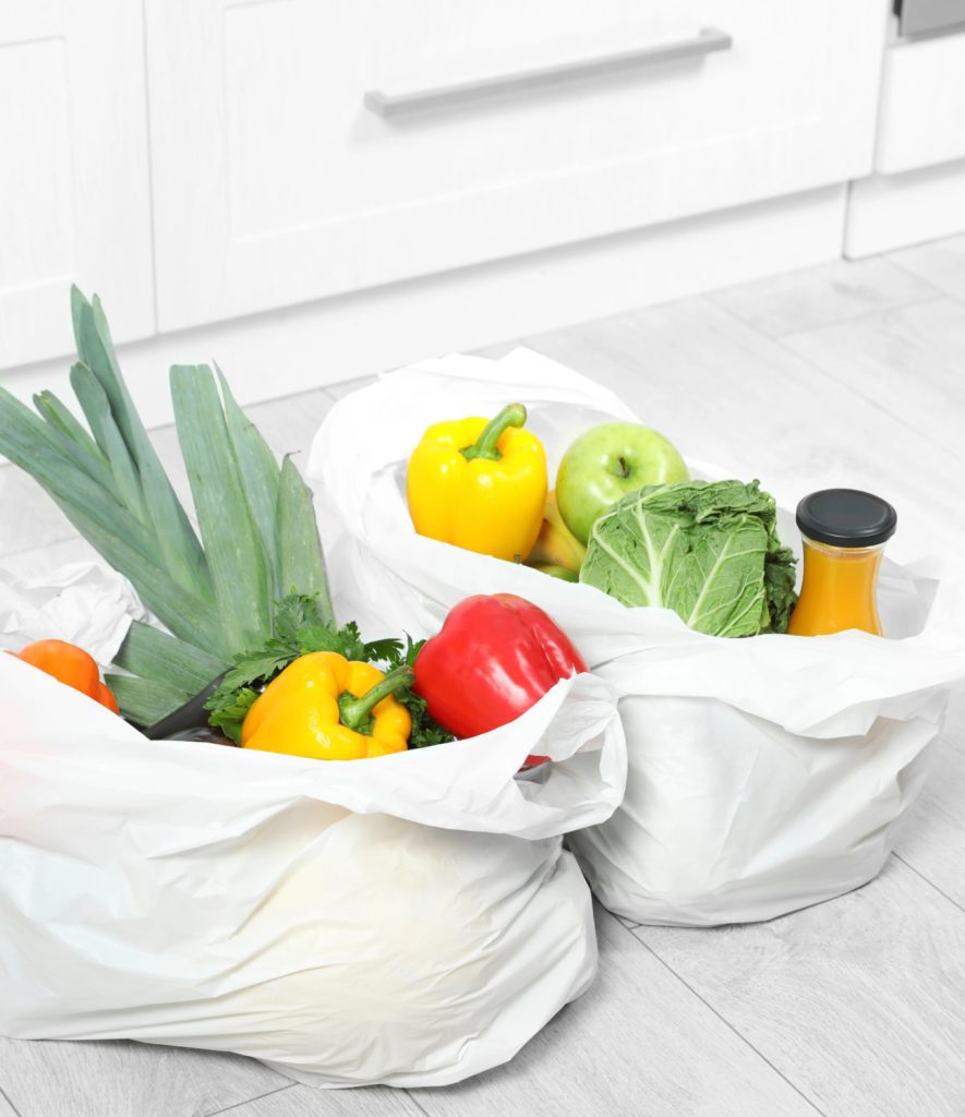 2 white plastic bags of groceries on a pantry floor