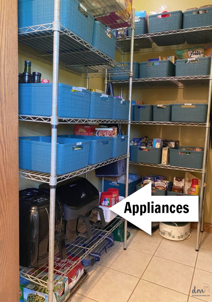 A walk in pantry with blue baskets on the shelves and small appliances stored on a lower shelf 