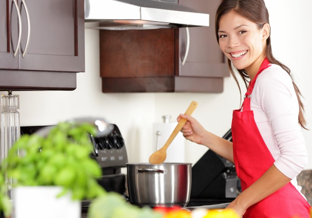 a woman in a red apron cooking at a stove in a kitchen