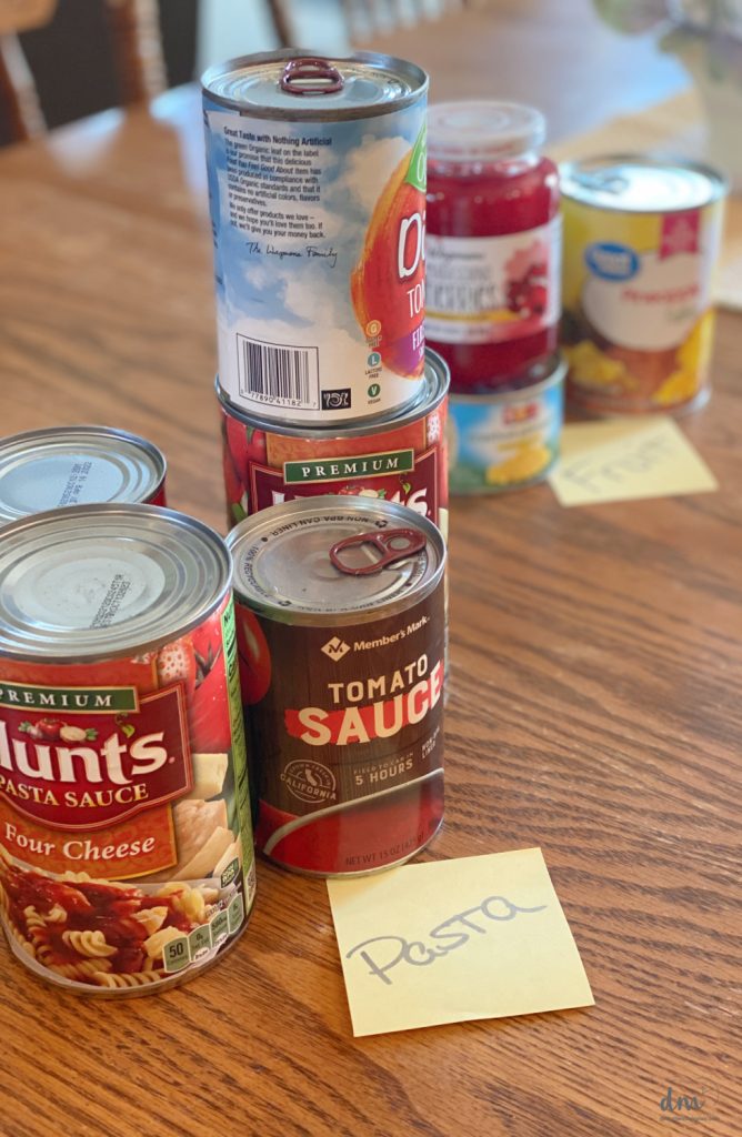 canned goods sorted into categories on a kitchen table with PASTA on a sticky note