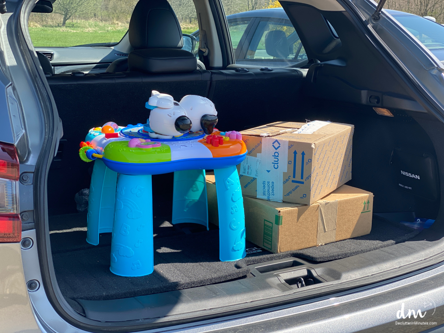 The trunk of a car filled with donation boxes and a colorful baby activity table