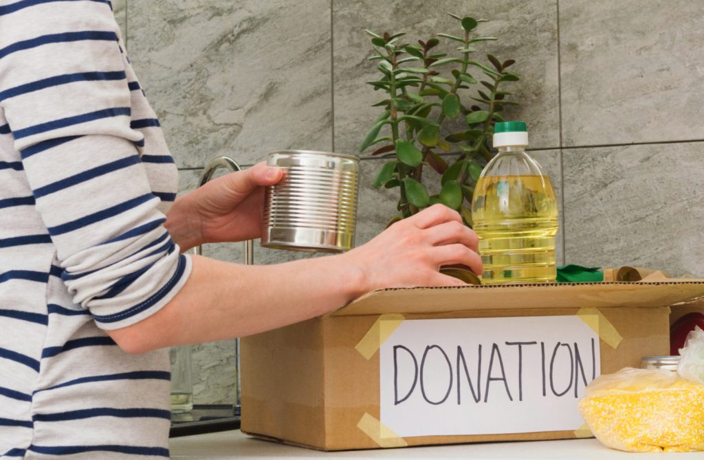 hands putting excess food into a cardboard box labeled donation