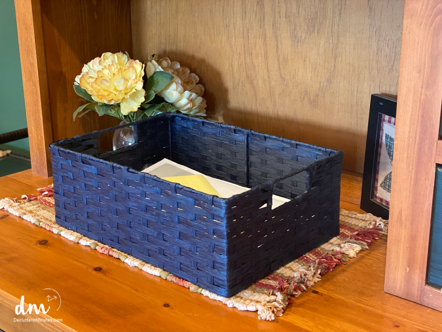 A navy blue woven basket holding papers on a wooden shelf