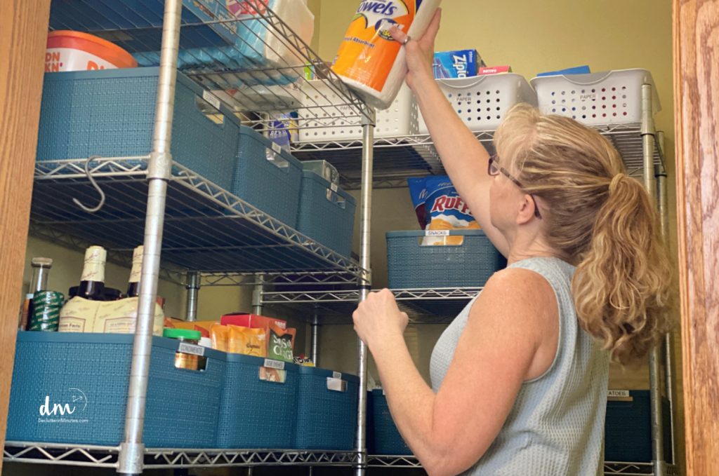 woman putting a roll of paper towels onto a pantry shelf