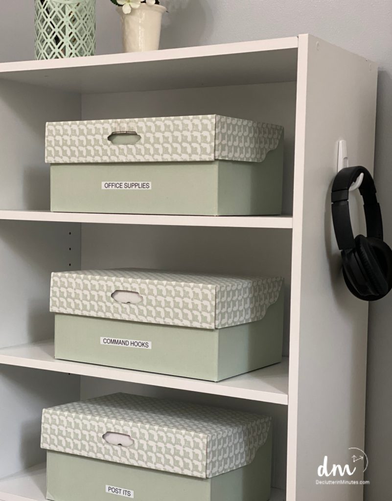 A white shelf with labeled storage boxes for office supplies and command hooks
