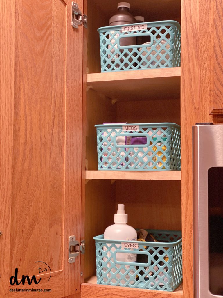 a cabinet in a kitchen with 3 blue baskets labeled eyes, meds, first aid
